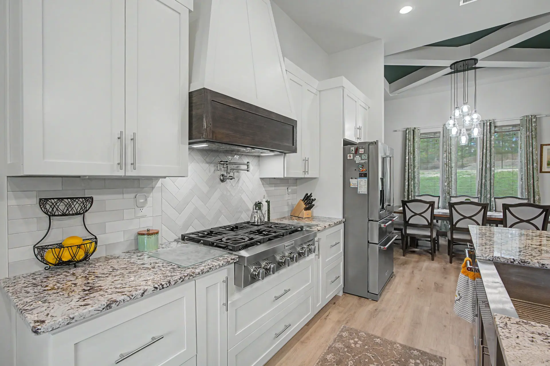 Kitchen range wall with custom hood, herringbone tile backsplash, and pot filler