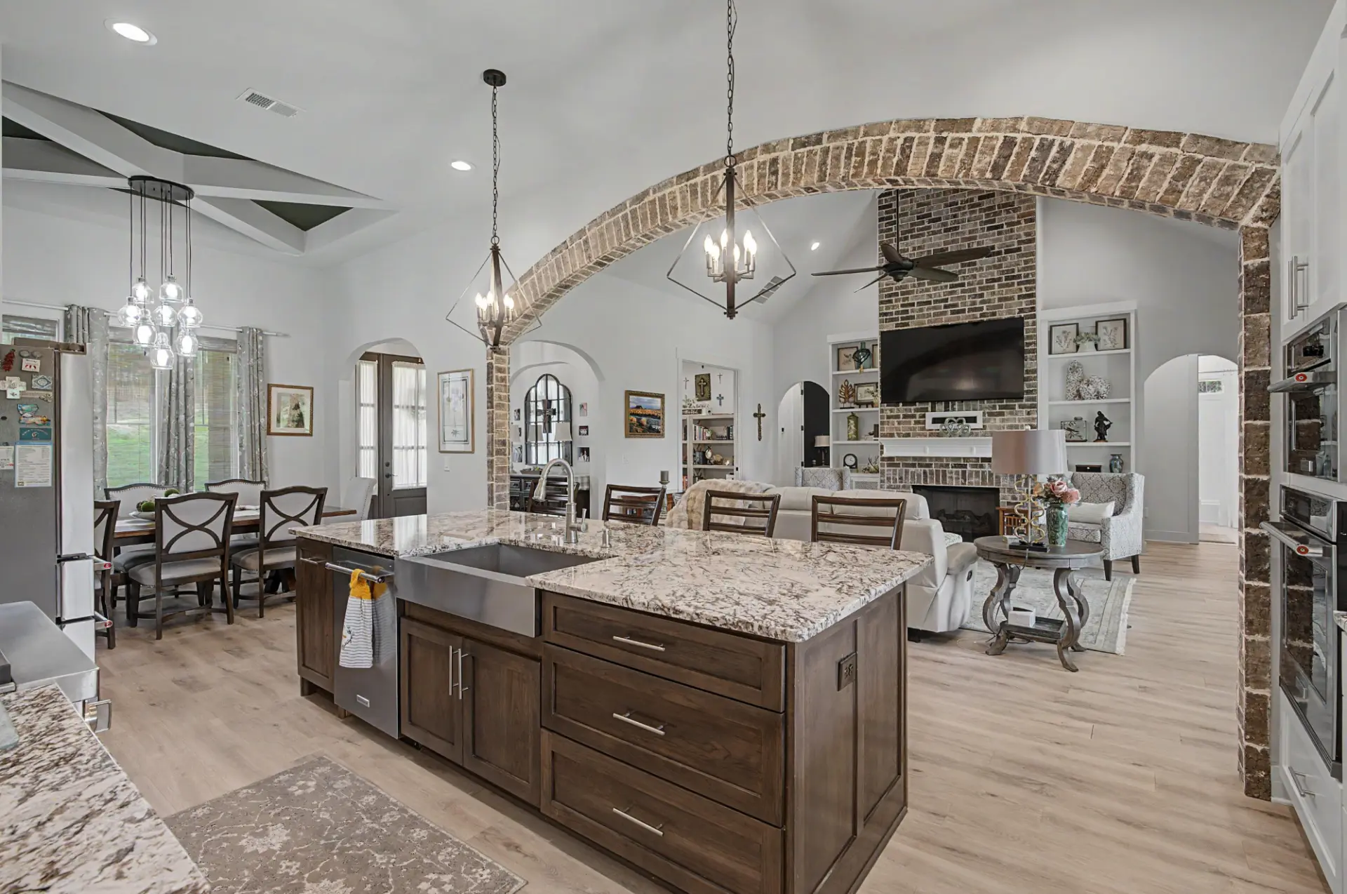Open kitchen with stained wood island, granite counters, and brick archway into the living room